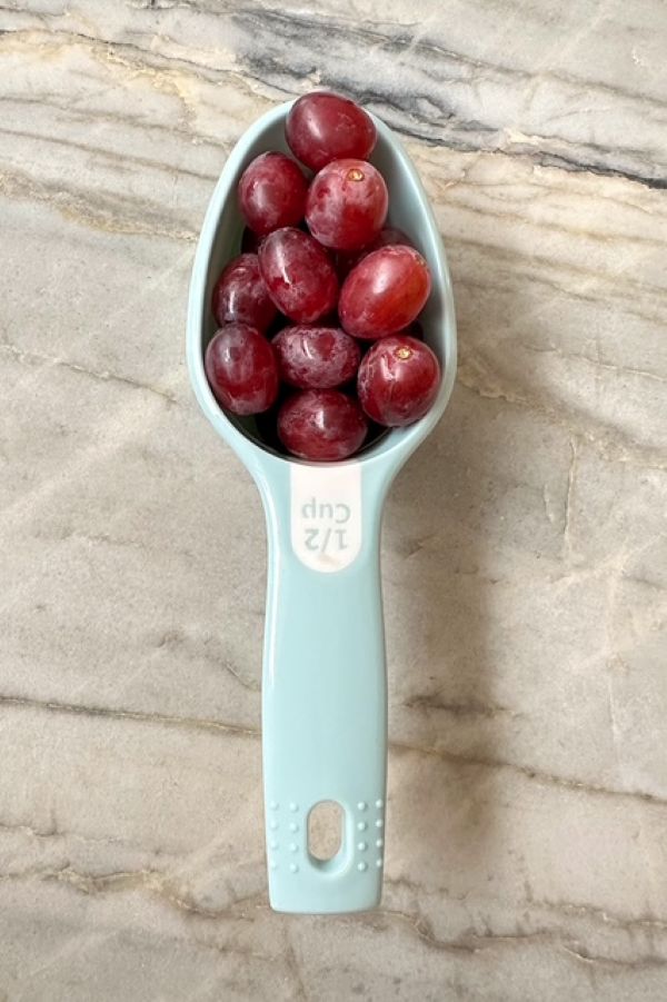 A light blue half cup measure holds red grapes.