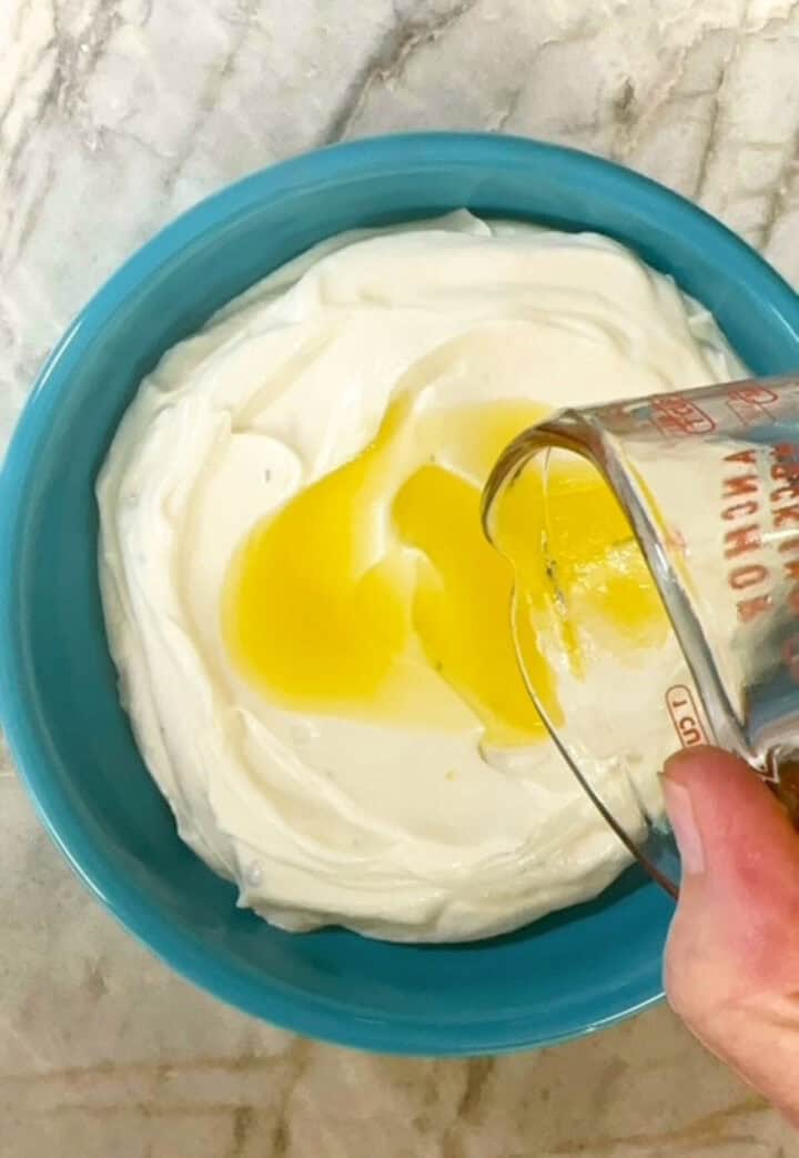 A golden olive-oil and honey topping is poured from a measuring cup onto creamy white ricotta dip.