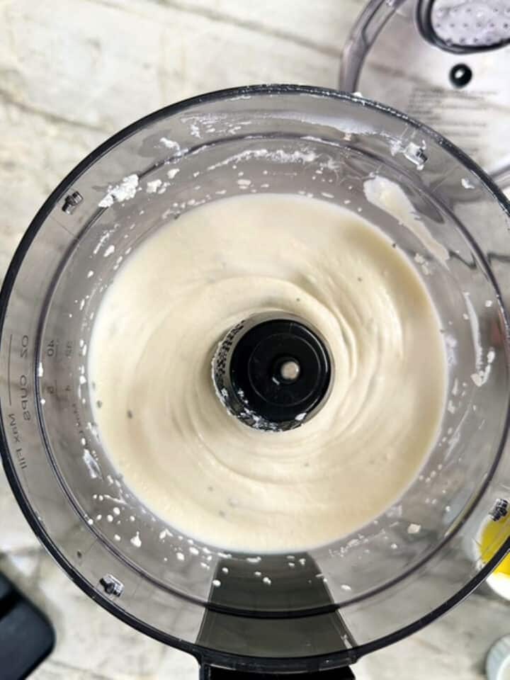 Smooth white paste made of ricotta cheese in food processor bowl with black circle center.