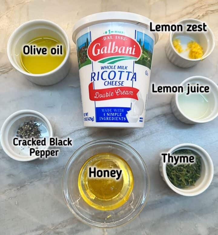 A group of ingredients on a marble counter with ricotta cheese, honey, olive oil, etc. for a dip recipe.