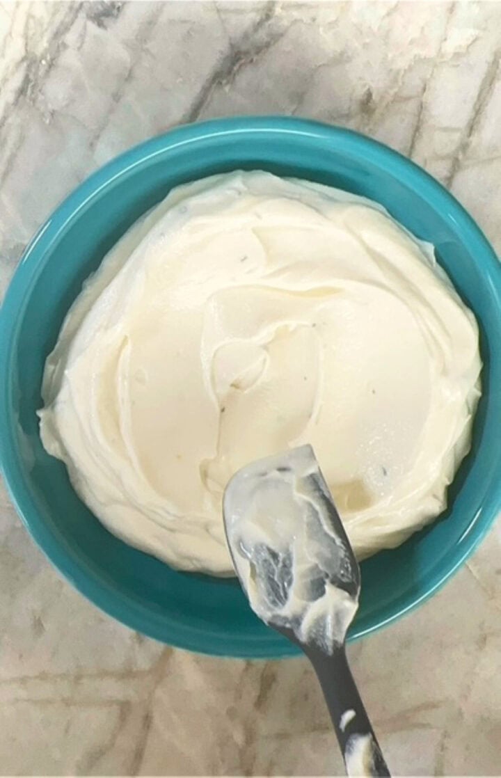 Creamy, white honey ricotta dip fills a blue-green bowl and has an indentation in the middle of the cheese dip.