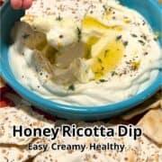 A hand dips a cracker into a creamy dip in a green bowl.