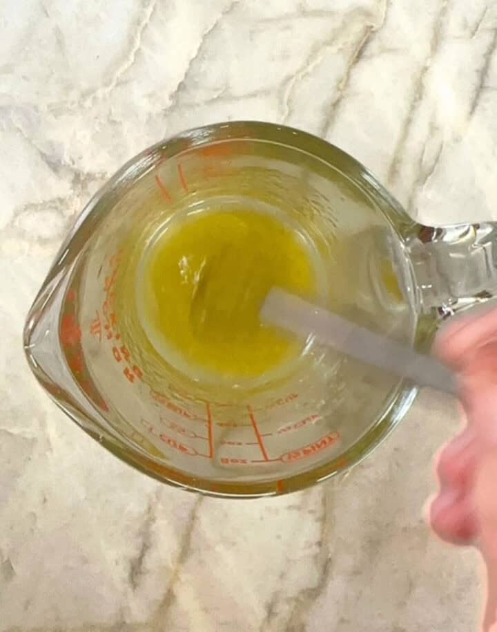 In a glass measuring cup, olive oil and honey are whisked together to make a light green liquid.