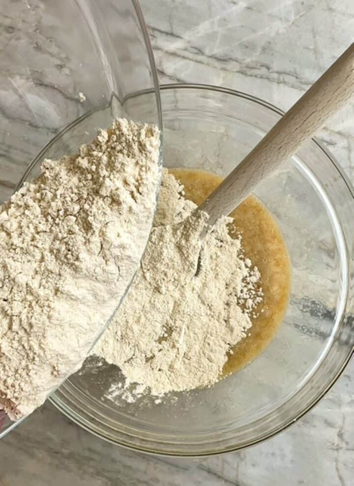Floury white dry ingredients are sprinkled over liquid banana ingredients for muffin making.