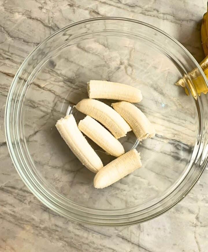 A large clear bowl holds halves of three creamy bananas.
