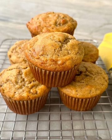 Half a dozen golden brown gluten free banana muffins are stacked on a wire cooling rack.