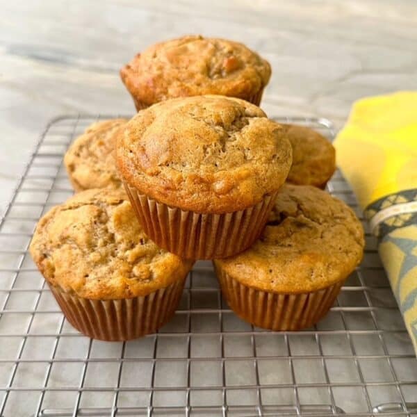 Half a dozen golden brown gluten free banana muffins are stacked on a wire cooling rack.