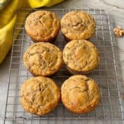 Half a dozen golden brown banana muffins (gluten-free) cool on a wire rack.