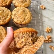Golden brown banana muffins with one coming out of it's brown parchment wrapper.