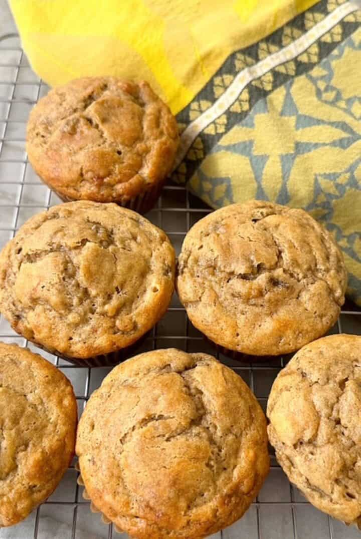 Several round, golden banana muffins are next to a gold and blue kitchen towel.