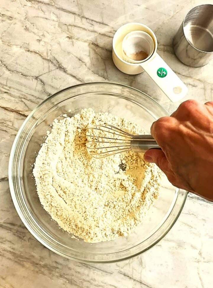 Creamy flour and other dry ingredients are whisked in a clear bowl.