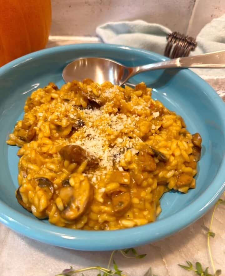 Shallow round turquoise bowl filled with golden and creamy Pumpkin Mushroom risotto.