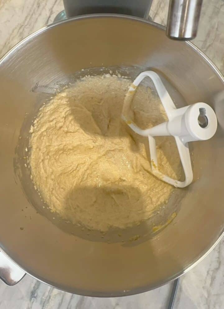 Metal stand mixer bowl with light colored sugar-fat mixture and white beater.