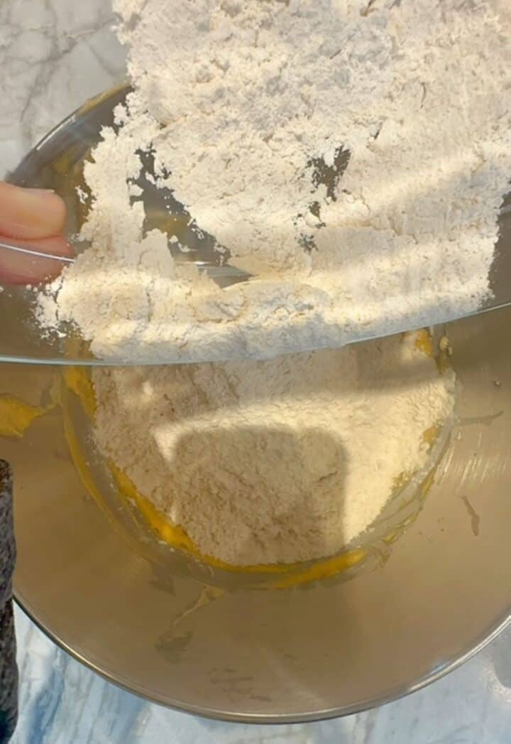 Light-colored flours plus spices are added to batter in the metal bowl of a stand mixer.