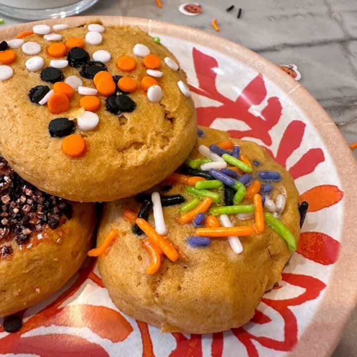 Patterned orange and white plate with three amber pumpkin ricotta cookies covered in Halloween sprinkles.