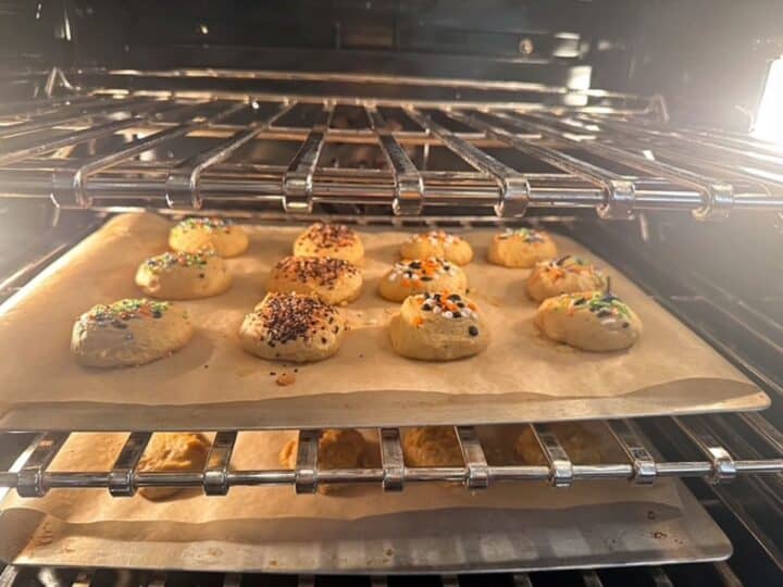 Light shines in a dark oven to show two baking sheets full of golden pumpkin cookies.