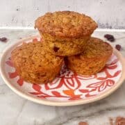 Stack of 3 pumpkin baked oatmeal cups on a white and orange plate with dried cranberries on the counter.