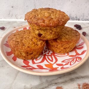 Stack of 3 pumpkin baked oatmeal cups on a white and orange plate with dried cranberries on the counter.