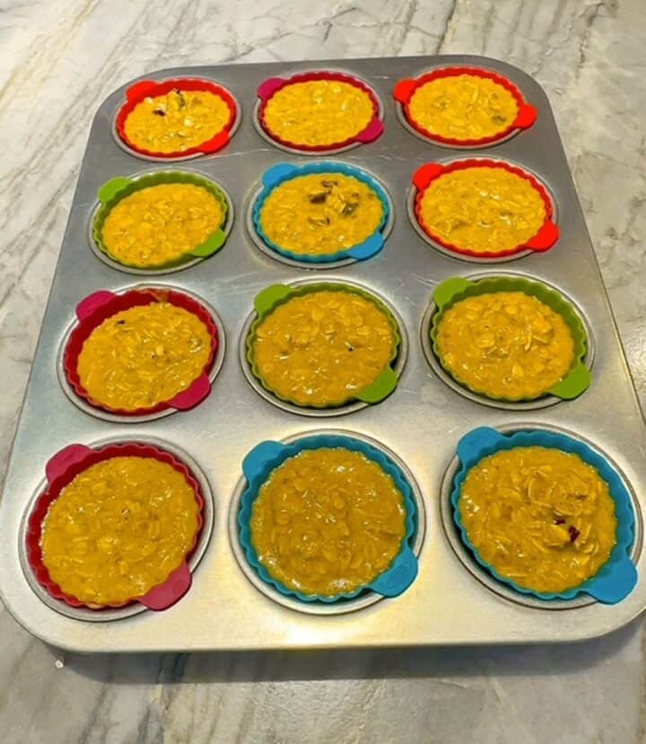 A metal 12-cup muffin tin with batter-filled blue, green, and red silicone liners ready for the oven.