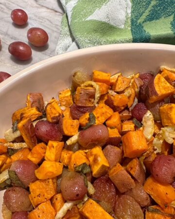 Orange sweet potatoes and dull purple grapes in an oval casserole dish with some fresh purple grapes off to the side.