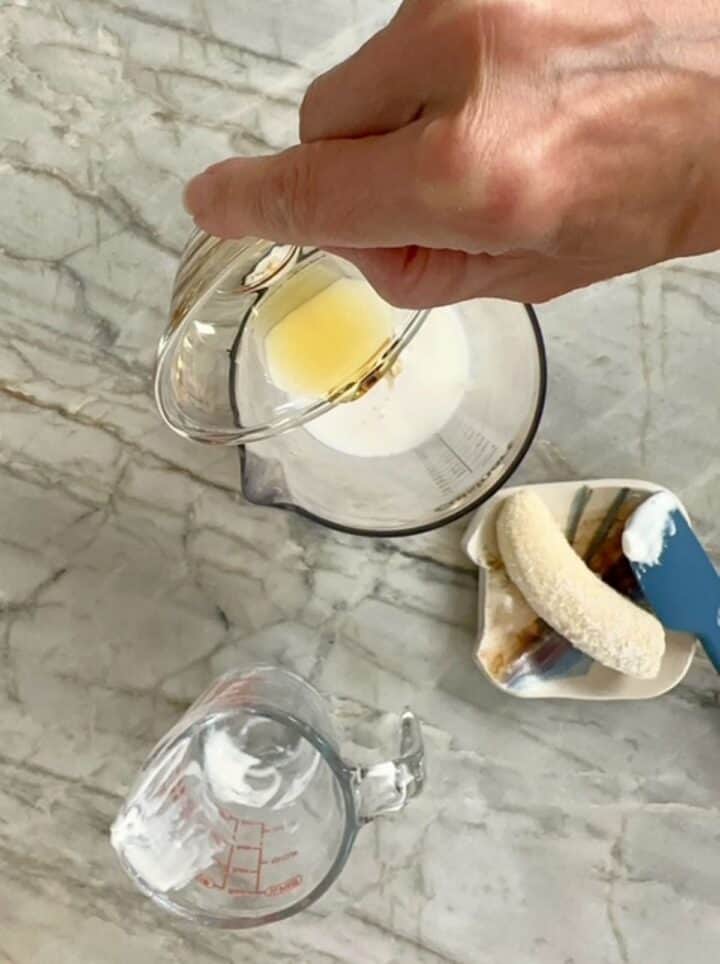 Pouring golden maple syrup into a high-sided clear container with yogurt for a peanut butter smoothie.