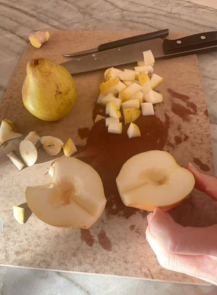 Pears chopped, cored, and cut in half on a brown cutting board.