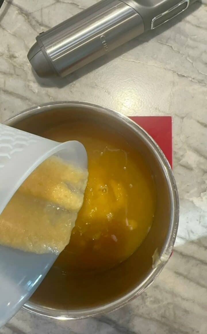 Yellow pear puree is poured from a white opaque container into a saucepan of liquid.