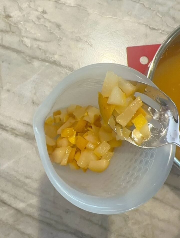 Metal slotted spoon transfers soft yellow pears to a large opaque high-sided container.