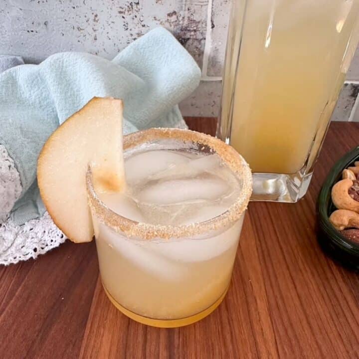 Round glass with sugared rim and garnish full of honey-colored liquid sits on a brown wooden surface.