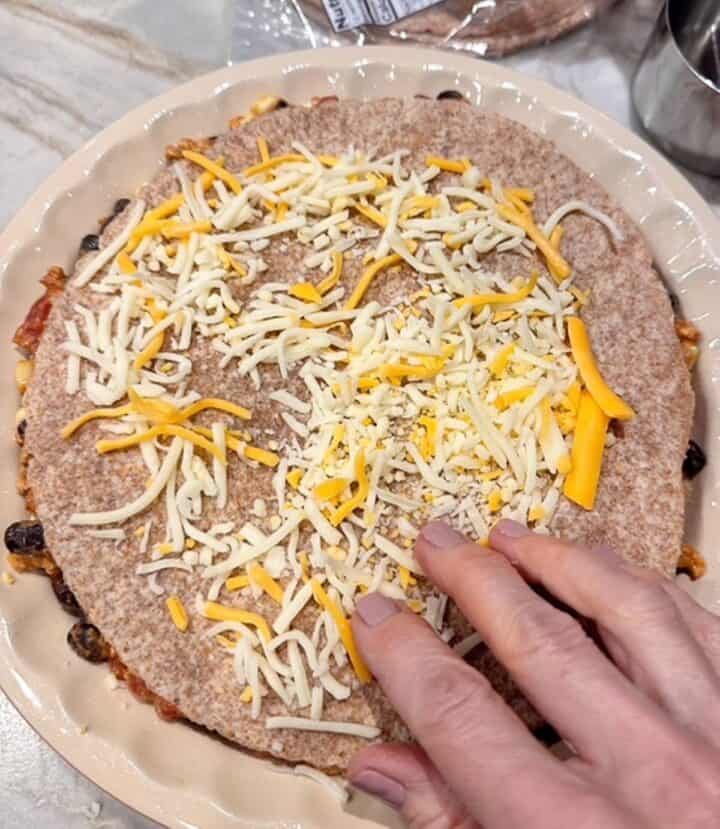 Brown wheat tortilla sprinkled with orange and white cheese over meat-bean-corn filling in a pie dish.