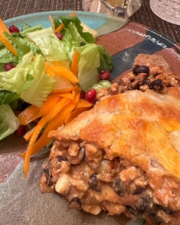 Turquoise and brown pottery dinner plate with green salad and ground meat and black bean taco pie topped with melted orange cheese.
