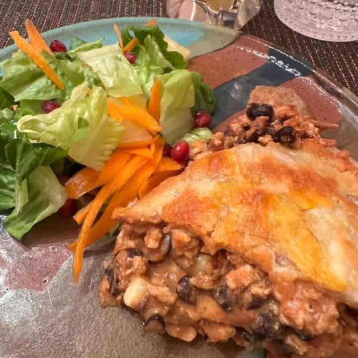 Turquoise and brown pottery dinner plate with green salad and ground meat and black bean taco pie topped with melted orange cheese.