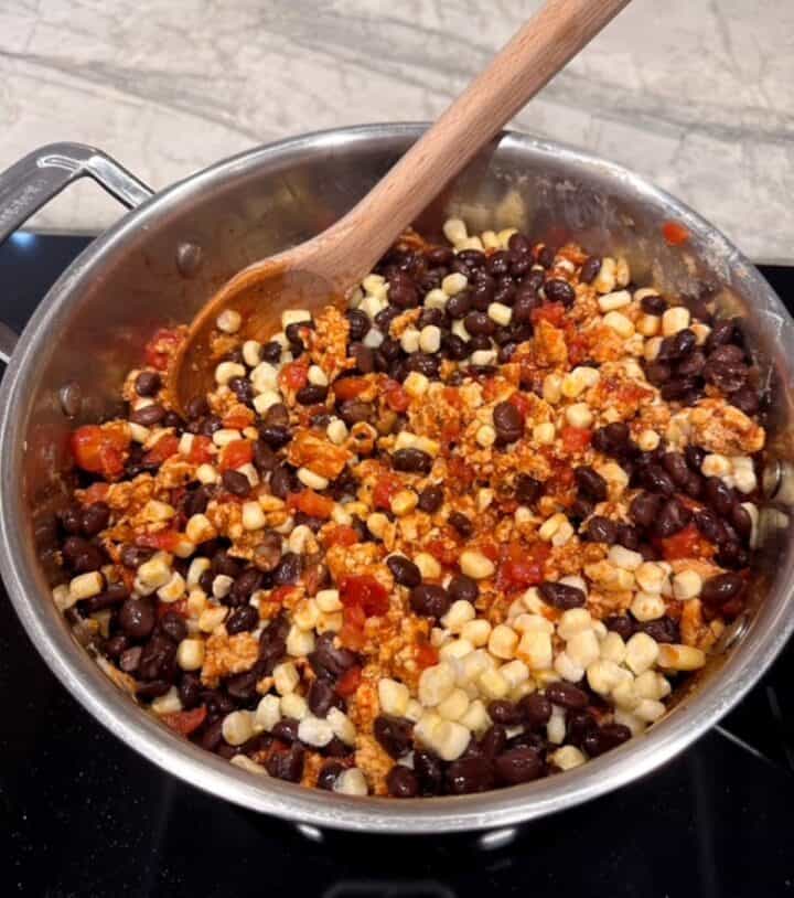 A mix of taco-spiced ground meat, tomatoes, black beans, and corn in a silver metal skillet.