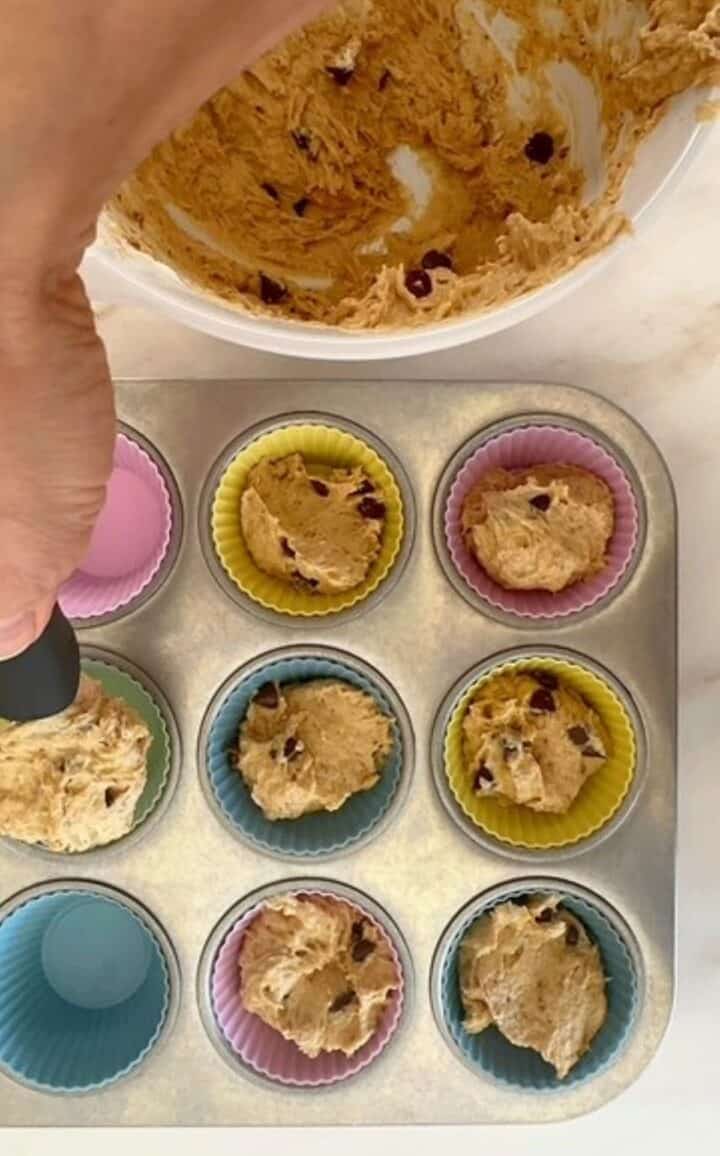 Transferring sticky peanut butter muffin batter to colorful liners for baking in a muffin tin.