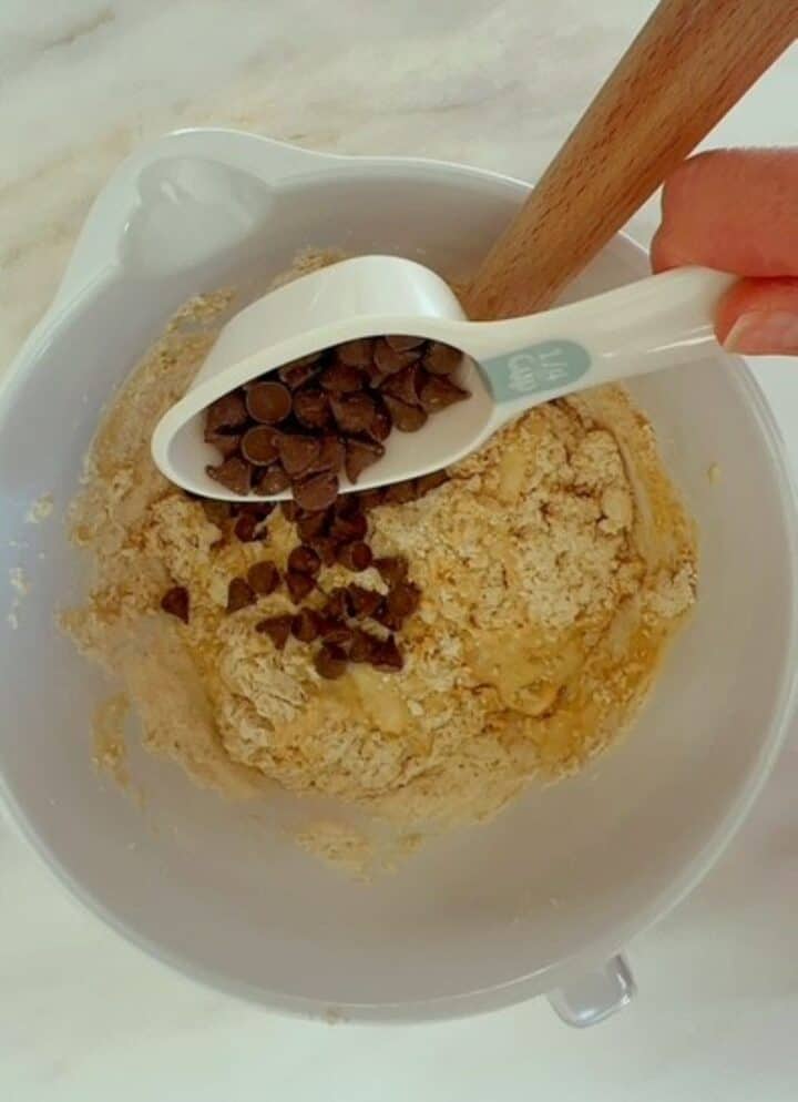Dark brown chocolate chips are poured into banana peanut butter muffin batter.