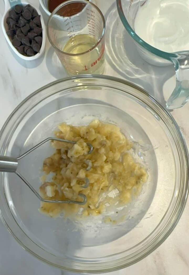 Mashing a yellow banana in a clear bowl for peanut butter powder muffins.