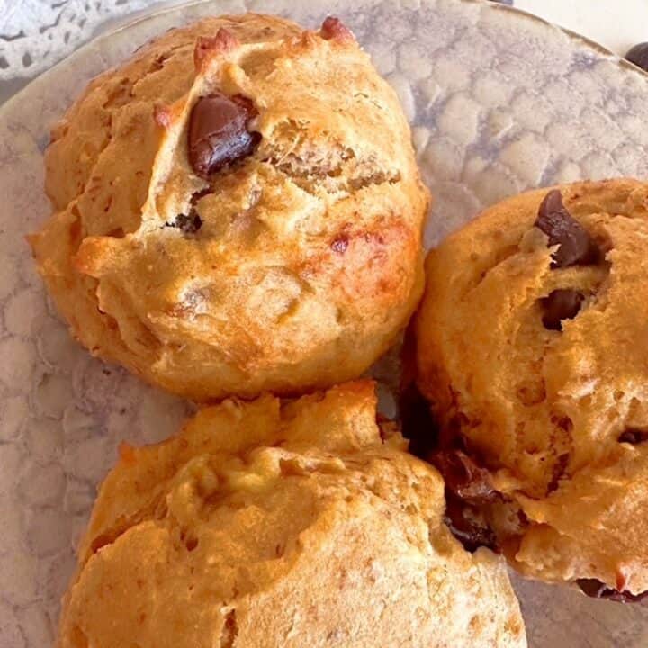 Closeup view of three round, chocolate-chip studded banana peanut butter muffins on a pastel pottery plate.