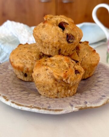 A lavendar pottery plate holds a stack of four golden peanut butter banana muffins.