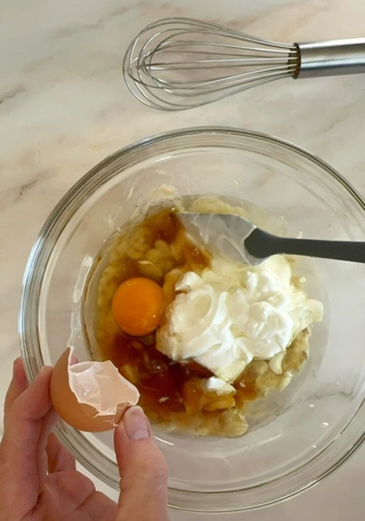 Clear bowl of liquid ingredients like white Greek yogurt and a raw egg needed for peanut butter powder muffins.