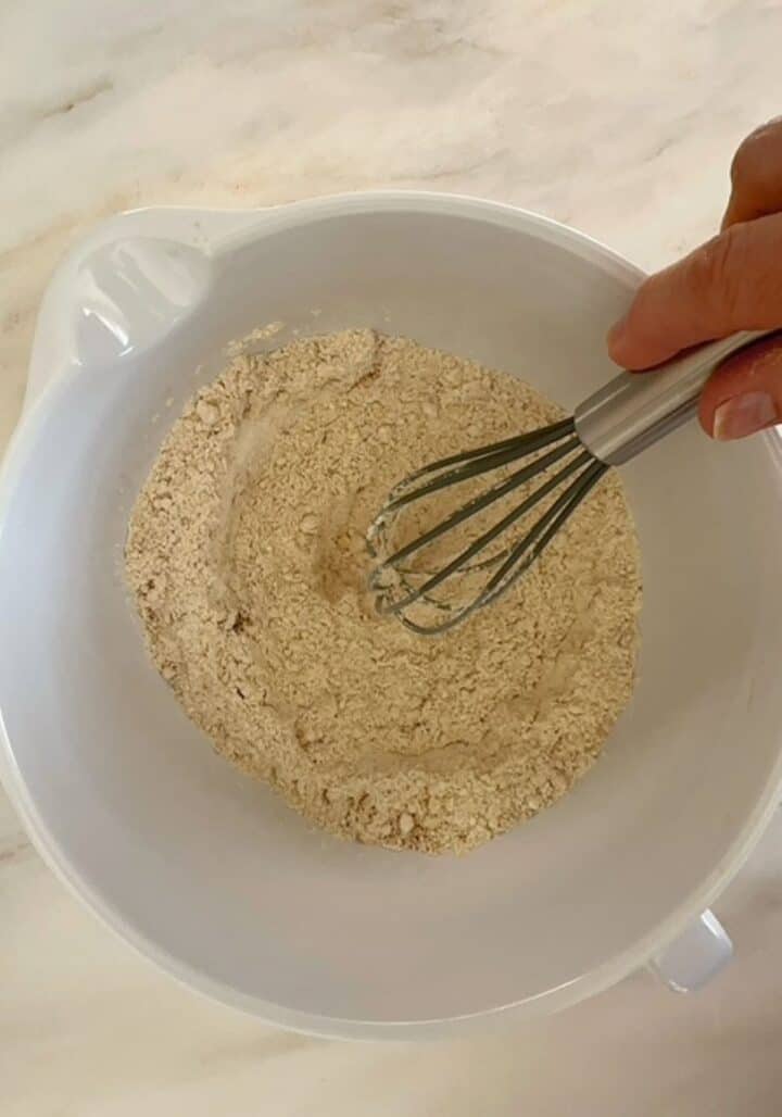 Golden colored, floury dry ingredients being whisked for peanut butter powder muffins in a white bowl.