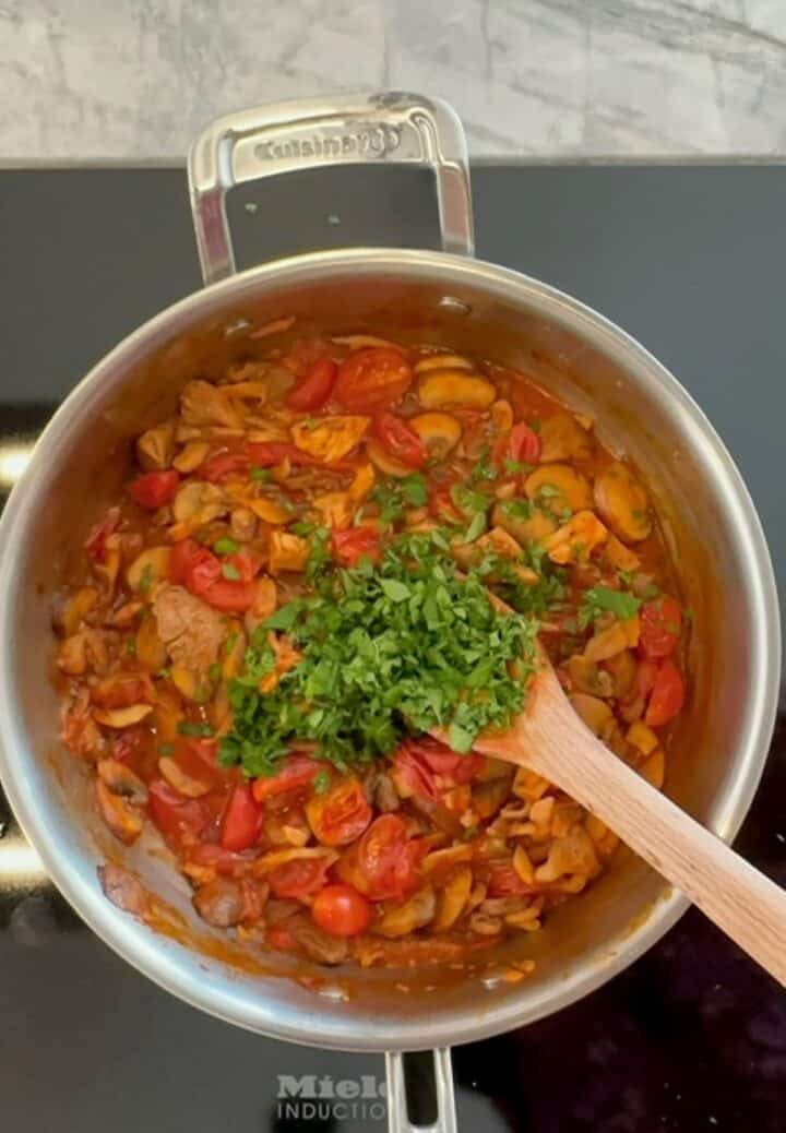 A bright green mound of chopped parsley added to brown-red mushroom tomato sauce/topping for baked polenta.