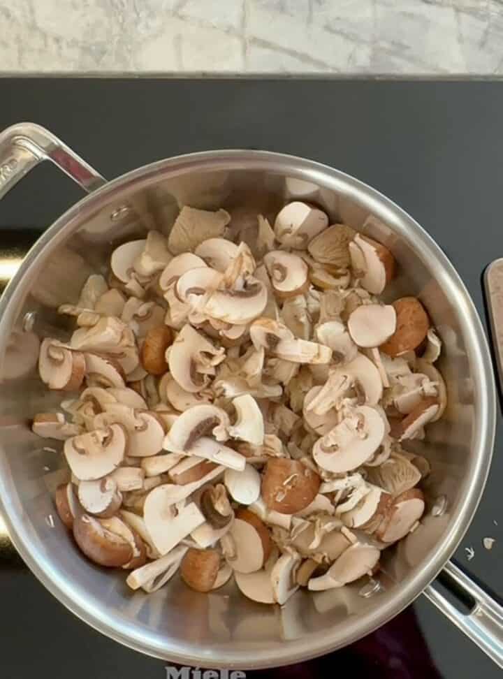 Cooking raw brown mushrooms in a large skillet to start topping for creamy baked polenta.