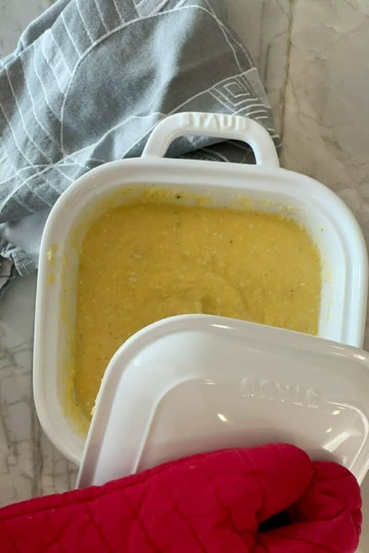 A white lid is placed over creamy yellow baked polenta in a white casserole dish.