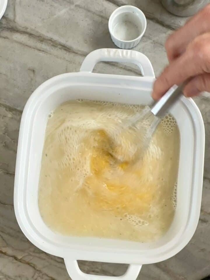 Whisking raw cornmeal into white casserole dish to start creamy baked polenta.