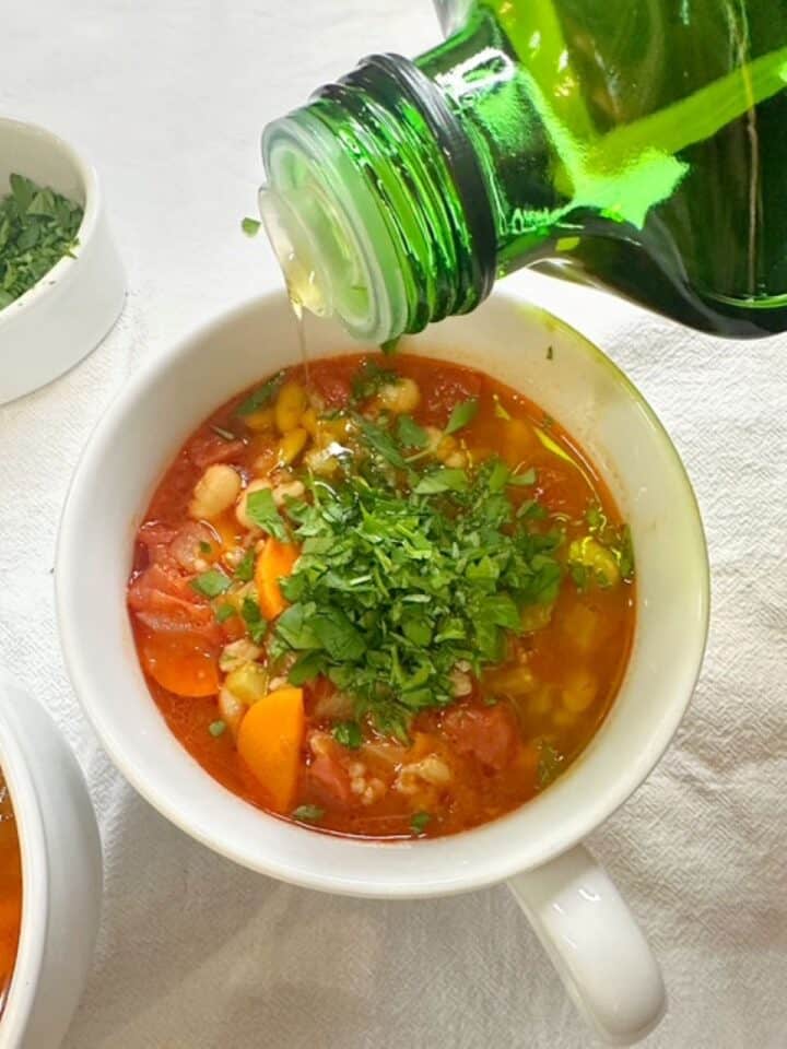 Olive oil is drizzled onto red-orange farro soup with visible orange carrot slices.