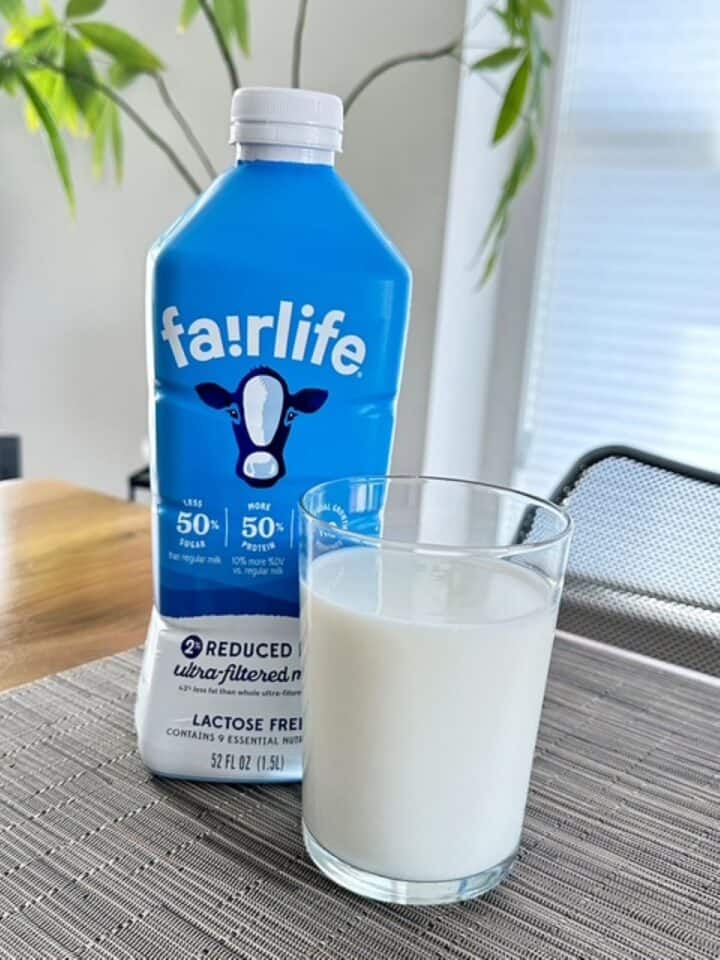 Blue bottle of fairlife ultra-filtered milk next to a tall, clear glass of white milk.