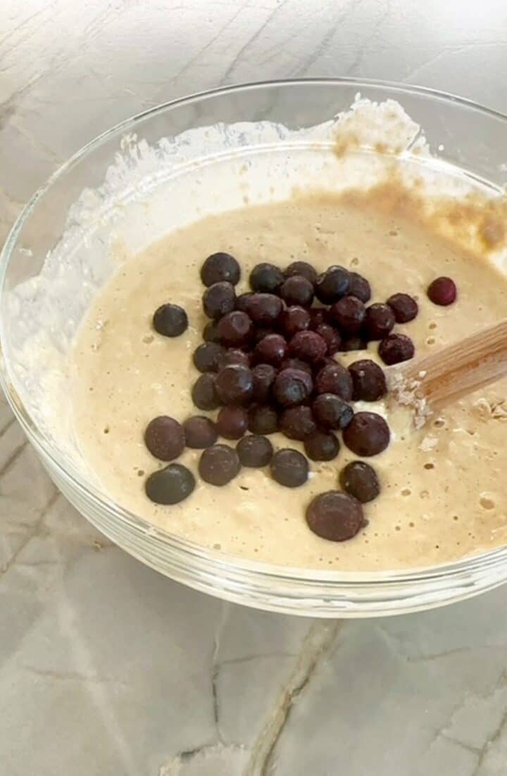 Clear bowl of pancake batter with dark blueberries on top.