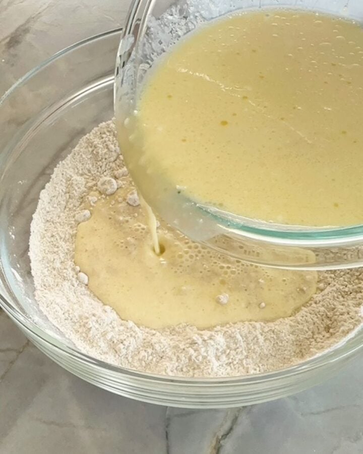 Pouring creamy yellow wet ingredients into flours, etc for protein sheet pan pancake batter.