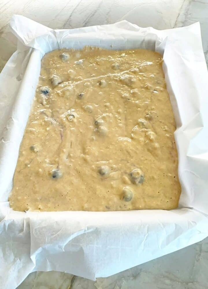 Parchment-lined sheet pan holds batter studded with blueberries.