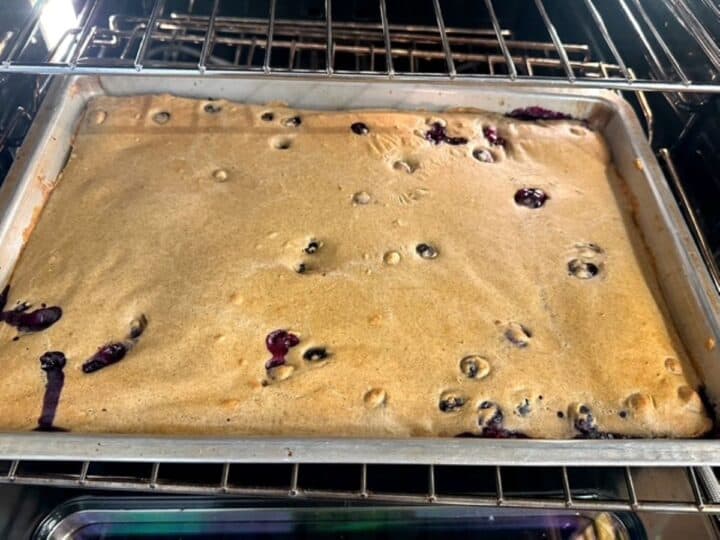 Golden sheet pan pancake with dark juicy blueberries baking in the oven.